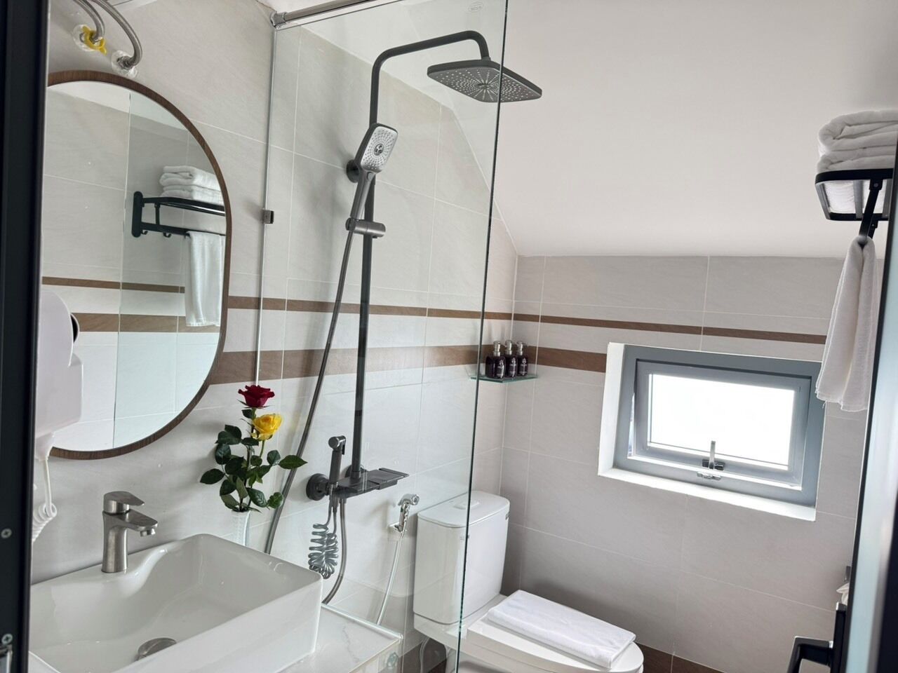 A bathroom with a shower, toilet, sink, and a window.