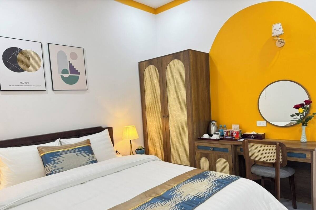 A hotel room with a bed, a desk, a chair, a mirror, and two framed artworks on the wall.