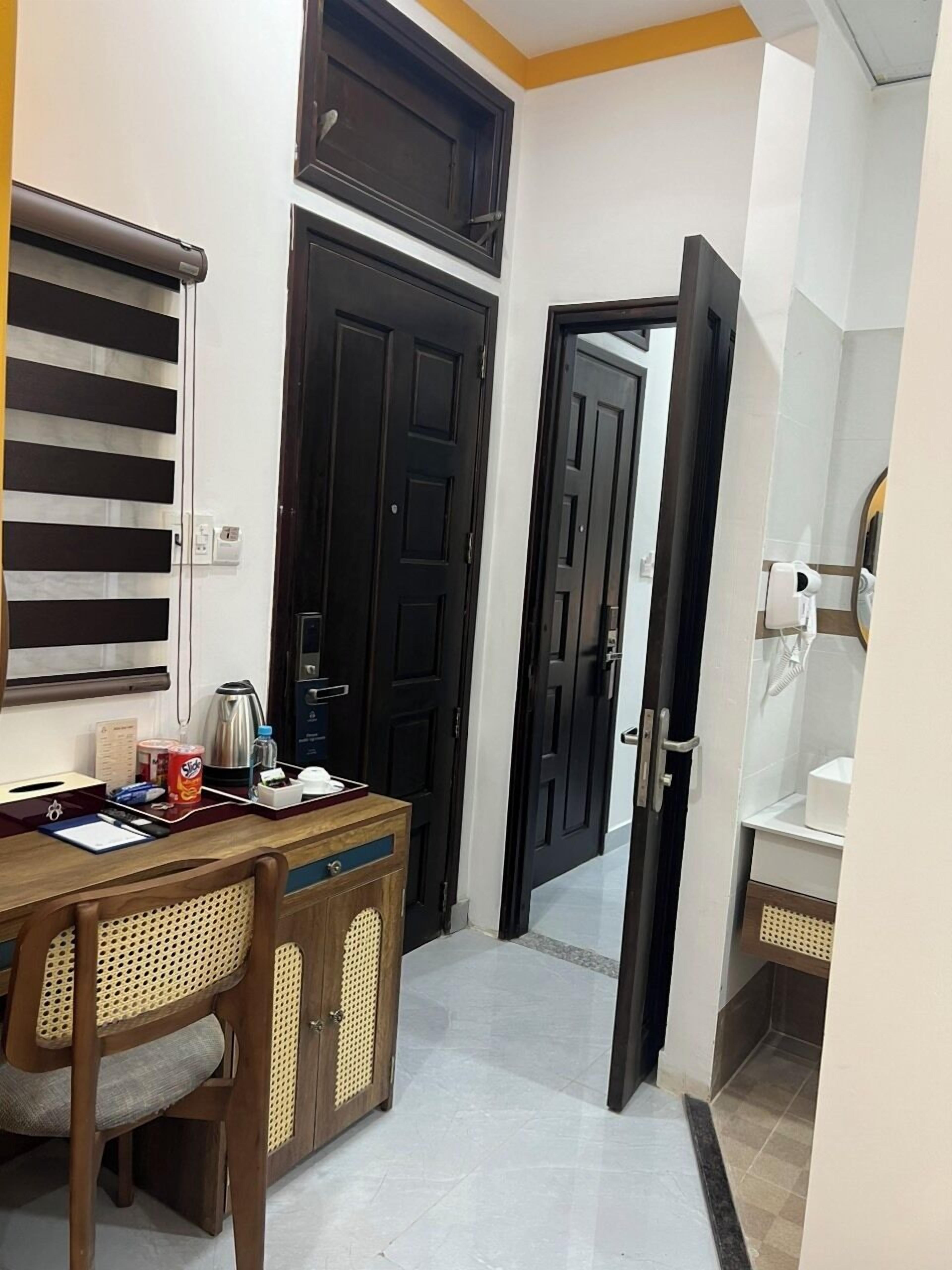 A hotel room with a wooden desk, chairs, a black door, and a bathroom with a mirror and sink.