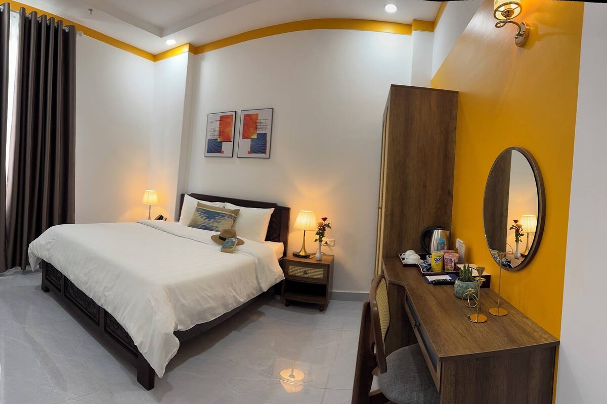 A hotel room with a bed, bedside lamps, a dresser, a mirror, and artwork on the wall.