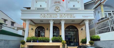 Un hotel con entrada central, una bandera y dos coches estacionados.