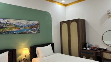Quarto de hotel com duas camas, um quadro de paisagem montanhosa, um guarda-roupa, uma escrivaninha com espelho e uma luminária.