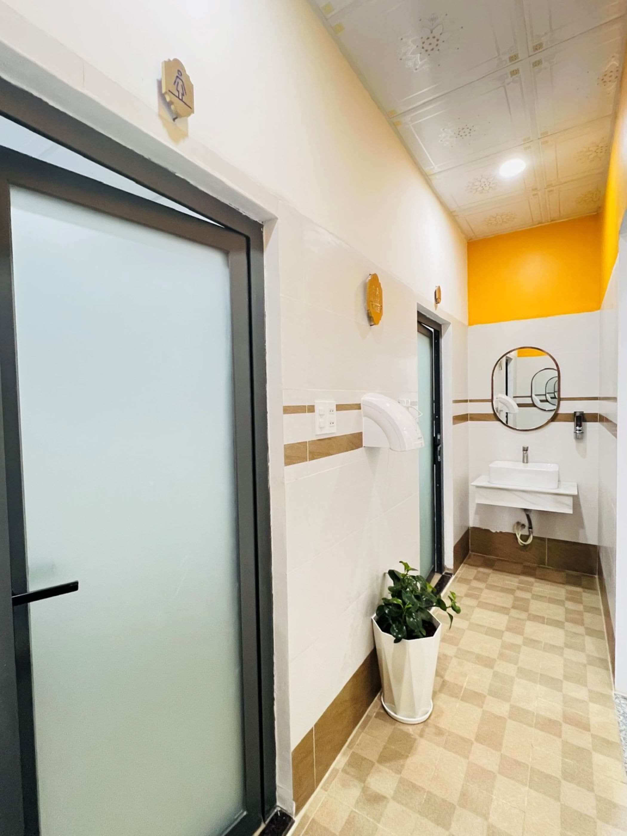 A hotel bathroom with a white sink, a mirror, and a potted plant.