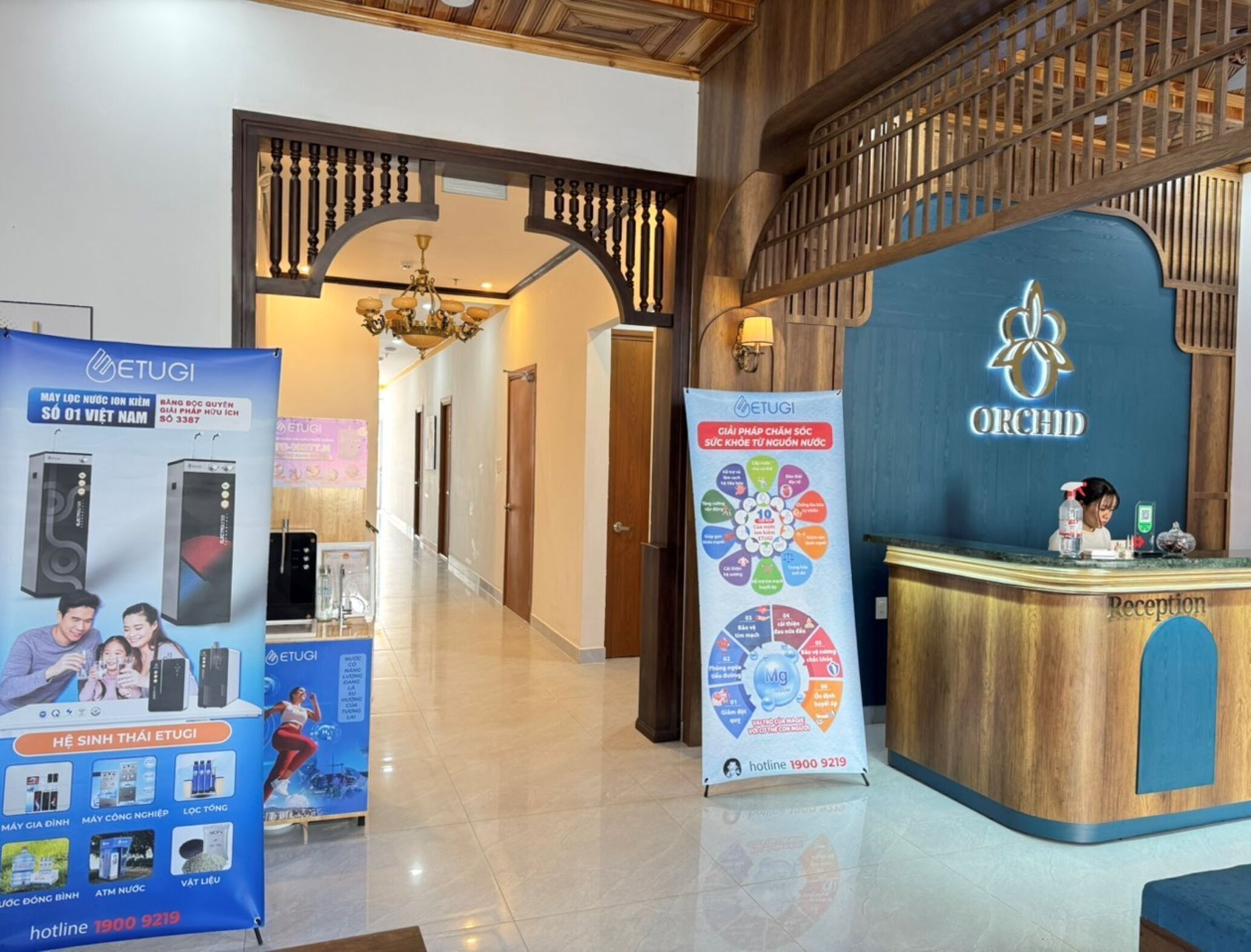 A hotel reception area with a reception desk, a chandelier, and a blue sign with the hotel name 'ORCHID'.