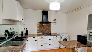 Cuina petita amb armaris blancs, forn de sobre, rentadora i un solll d'aixeta.