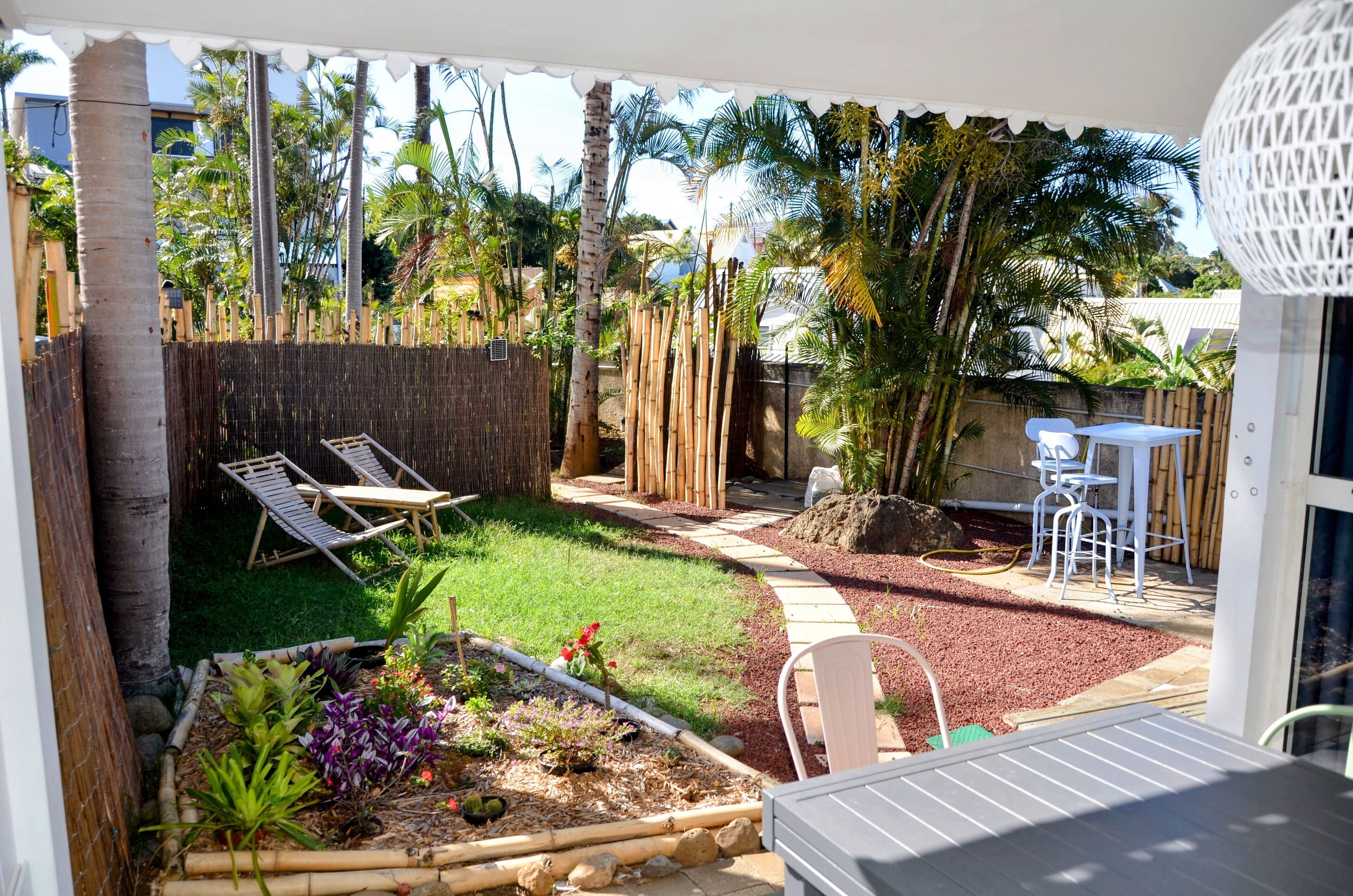 A patio with a bamboo fence, a small garden, and a seating area with chairs and a table.