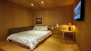 Een slaapkamer met een bed, een nachtkastje met een lamp, een aan de muur bevestigde televisie en een ingelijste foto.