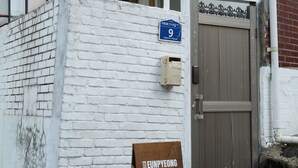 Een gevel met witte bakstenen, een metalen poort en een blauw bord met het nummer 9.