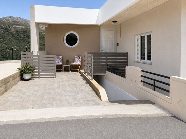 A modern building with a flat roof, a circular window, a door, and a small table with chairs.