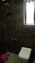 A bathroom with a shower, toilet, and a window.