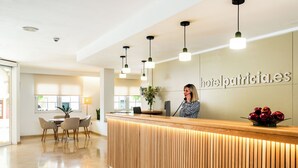 Un comptoir d’accueil d’hôtel avec un revêtement en bois et une enseigne indiquant « hotelpatricia.es ». Des lampes suspendues et une plante en pot sont posées sur le comptoir.
