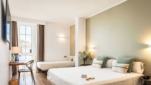 Une chambre d’hôtel avec deux lits, un bureau avec une chaise, une petite table avec une lampe et une fenêtre avec des rideaux.