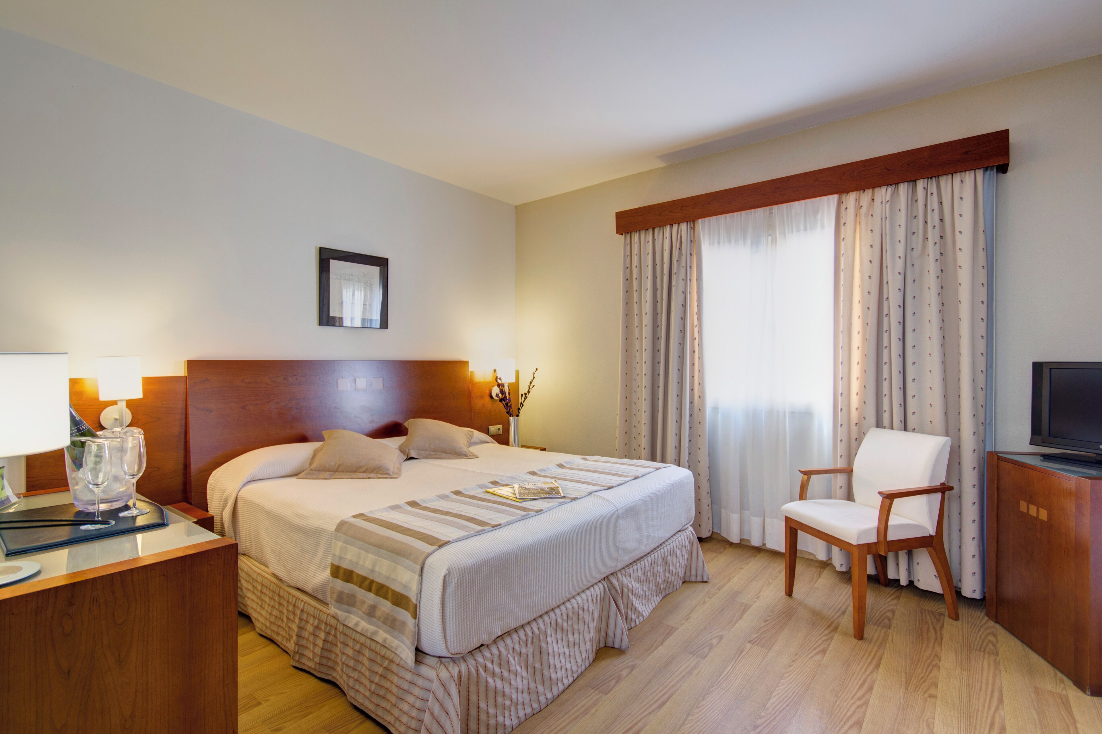 Habitación de hotel con una cama grande, cabecera de madera, escritorio con lámpara, una silla y televisión.