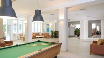 Una mesa de billar en una habitación amplia y luminosa, con muebles modernos y ventanas grandes.