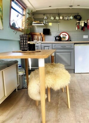 A compact kitchen with a wooden table, a fluffy stool, and various kitchen utensils hanging on the wall. - 5 Star Stunning Houseboat, no Experience Required! Enjoy the Most Romantic Trip! (Monasterevin)