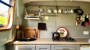 A compact kitchen with a sink, stove, and hanging mugs. - 5 Star Stunning Houseboat, no Experience Required! Enjoy the Most Romantic Trip! (Monasterevin)
