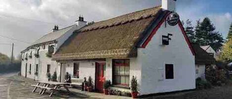 A white building with a thatched roof, a small porch, and a red door.