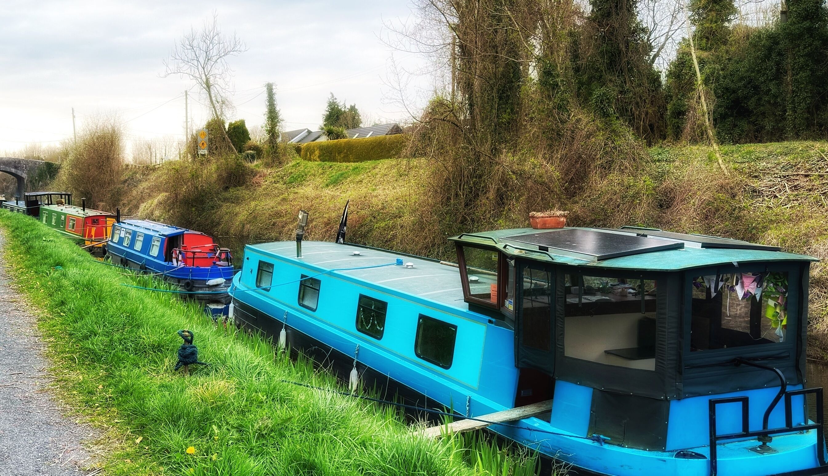 Une péniche à cabine bleue et noire, amarrée sur une berge herbeuse le long d’un canal.
