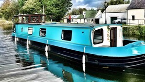 A narrowboat docked at a canal with a house and trees in the background. - 5 Star Stunning Houseboat, no Experience Required! Enjoy the Most Romantic Trip! (Monasterevin)