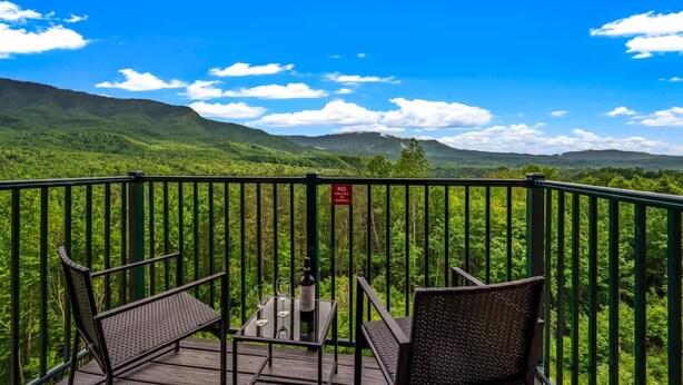 A balcony with a view of lush green mountains, a table with a bottle and glasses, and two chairs. - Full Kitchen Hot Tub Indoor Pool Sleeps 6 (Gatlinburg)