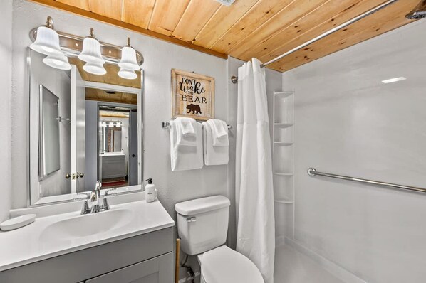 A modern bathroom with a wooden ceiling, a large mirror, a sink, a toilet, and a shower with a glass door.