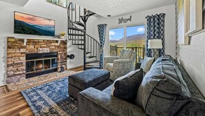 A living room with a fireplace, a spiral staircase, a sofa, and a large window with a view of the outdoors.