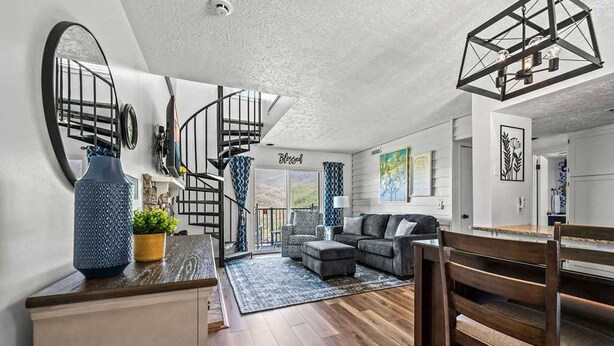 A modern living room with a sofa, ottoman, and dining table. A staircase leads to a balcony.