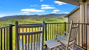 A balcony with two wooden chairs and a table, overlooking a mountainous landscape.