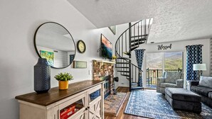 A modern living room with a wooden cabinet, a round mirror, a staircase leading to a balcony, and a view of the outdoors.