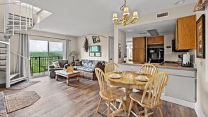 Un vaste espace de vie comprenant une table à manger pour quatre personnes, un canapé et un escalier menant à un balcon.