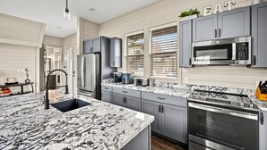 A modern kitchen with grey cabinets, a large island with a sink, a built-in oven, and a microwave. - NEW Lake View Indoor Pool Sleeps 14 Hot Tub (Sevierville)