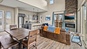 A spacious living area with a wooden dining table, a leather sofa, and a stone fireplace. - NEW Lake View Indoor Pool Sleeps 14 Hot Tub (Sevierville)