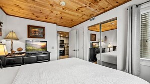Ein Schlafzimmer mit einem großen Bett, Holzboden, einem Fernseher und einer Schiebetür zu einem weiteren Raum.