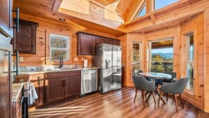 A wooden cabin interior with a kitchen, dining area, and large windows. - Mountain Views Sauna Hot Tub Fire Pit (Gatlinburg)