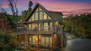 A two-story log cabin with a balcony on the upper level, surrounded by trees. - Mountain Views Sauna Hot Tub Fire Pit (Gatlinburg)