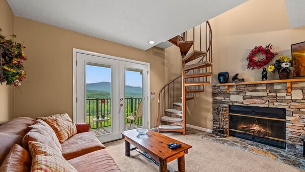 A cozy living room with a stone fireplace, a wooden staircase, and a balcony with a scenic view. - Hot Tub Heated Pool Mountain Views Sleeps 6 (Gatlinburg)