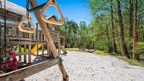 A wooden play structure with swings and a slide, surrounded by a forested area with picnic tables. - Hot Tub Heated Pool Mountain Views Sleeps 6 (Gatlinburg)