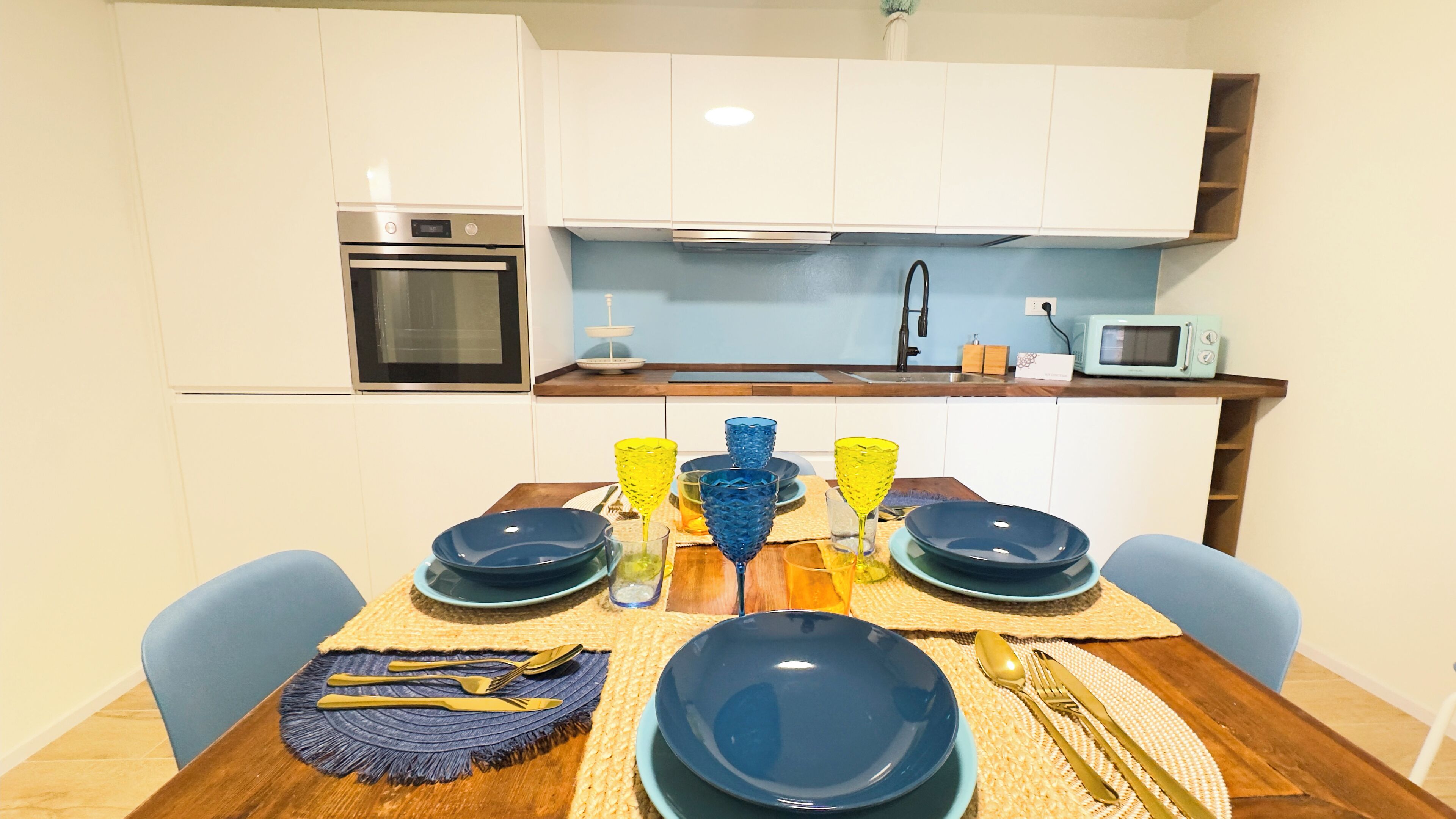 Una cocina compacta con armarios blancos, horno integrado, microondas y pileta.