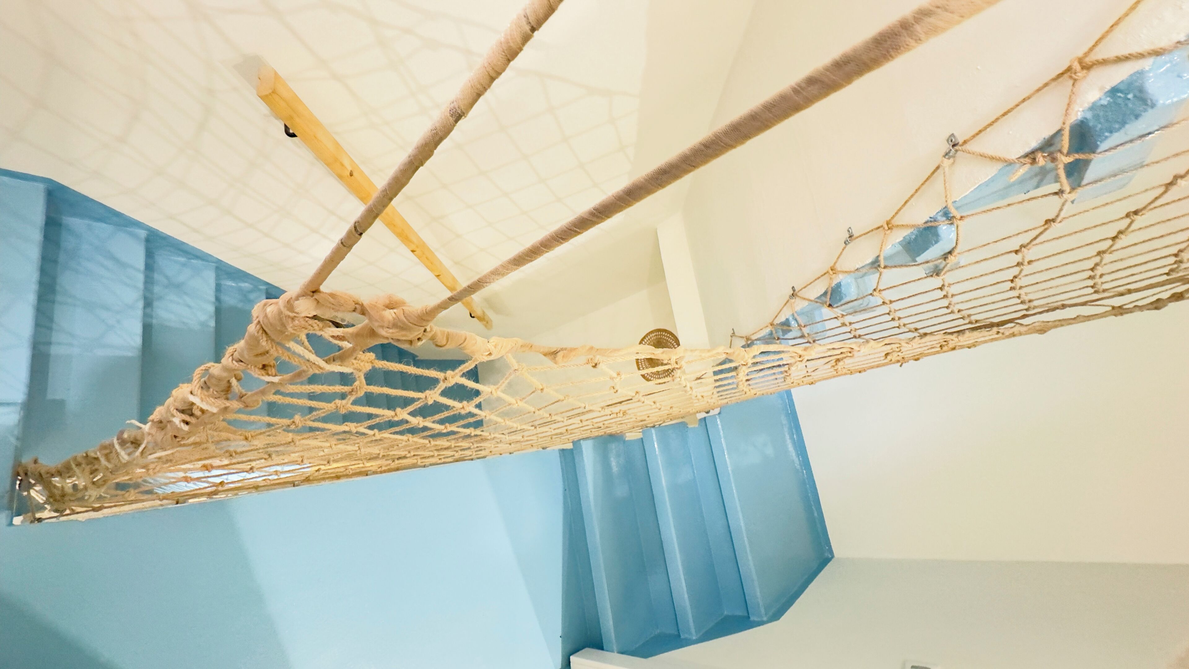 Een hangmat bevestigd aan het plafond in een kamer met blauwe gordijnen en een wit plafond.