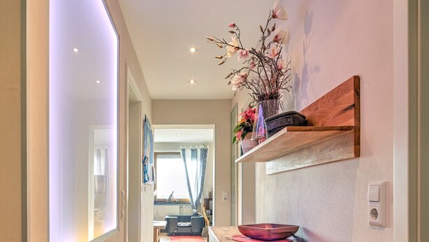 A hallway with a wooden counter, a patterned rug, and a view into a living area with a sofa and curtains. - Two-room PREMIUM apartment (Ostfildern)