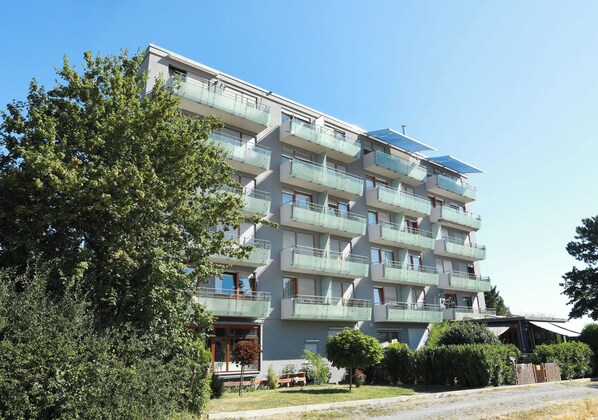A multi-story residential building with balconies, a solar panel on the roof, and a well-maintained lawn.