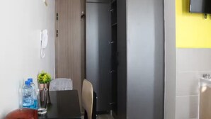 Une petite pièce avec une porte en bois, une petite table avec une chaise, une bouteille d’eau, un verre et une plante en pot.