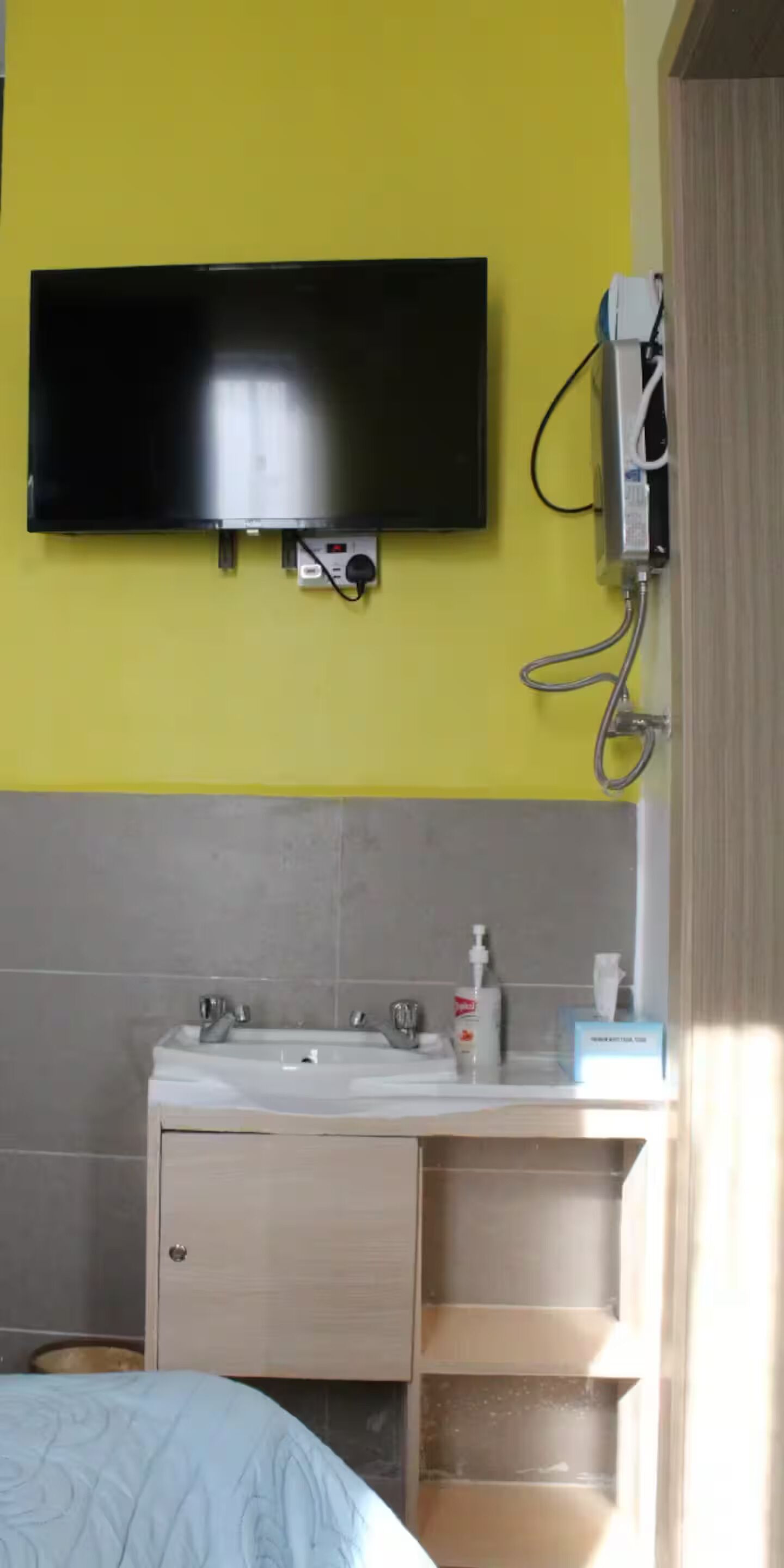 Een badkamer met een tv aan de muur, een wastafel met toiletartikelen en een bed met een blauwe sprei.