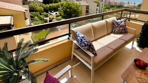 Un balcón con sofá y mesa, con vistas a la costa, edificios y zonas verdes.