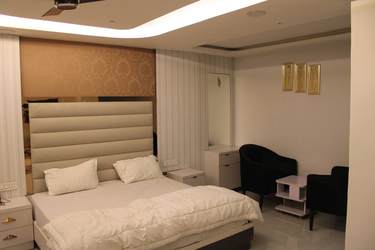 A modern bedroom with a large bed, bedside tables, a desk, a chair, and a ceiling fan.