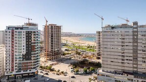 Ein Hochhaus mit mehreren Stockwerken, Baukränen und einem Strand im Hintergrund.