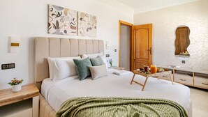 Ein modernes Schlafzimmer mit einem großen Bett, einem Nachttisch mit Pflanze, einem an der Wand befestigten Kunstwerk und einer Holztür.