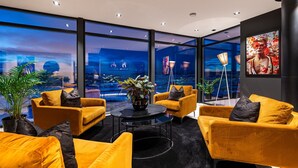 Un salón moderno con sofás amarillos, una mesa redonda negra y grandes ventanales que ofrecen vistas a la ciudad.
