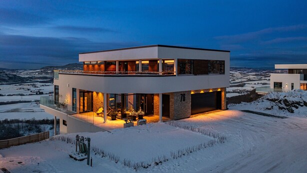Una casa moderna de dos pisos con un balcón grande, un garaje y vistas a un paisaje nevado.