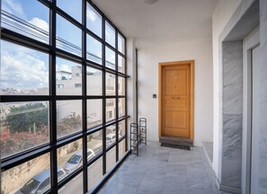 Un couloir doté de grandes fenêtres, d’une porte en bois et d’un sol carrelé.